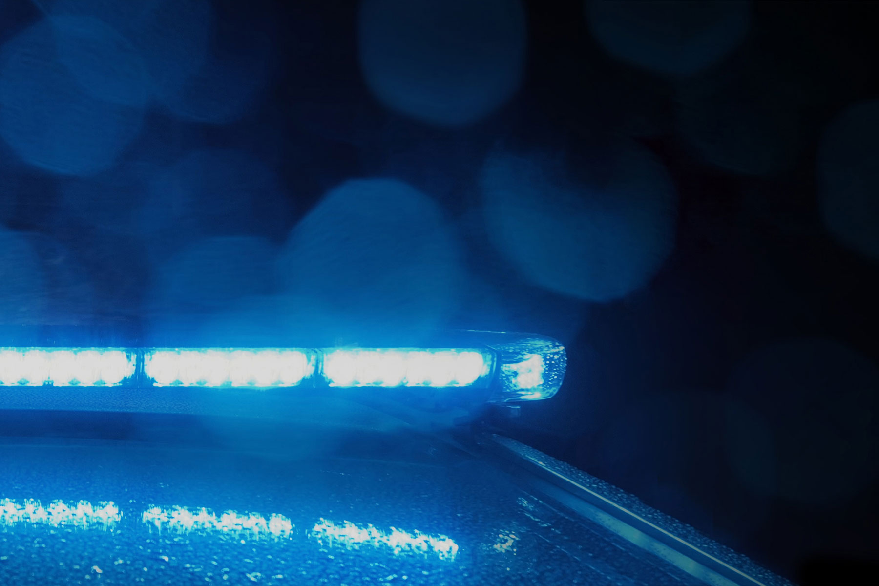 Page Image Lightbar Closeup at Night Lit Blue, Reflection on Vehicle Roof and Lens Flares in Foreground