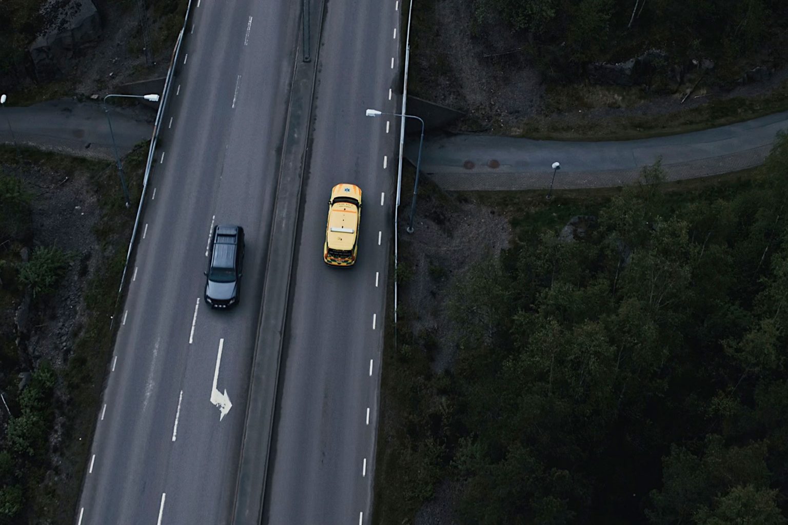 Page Image Aerial Motorway Shot Yellow Emergency Vehicle and Black Car Driving in Opposite Directions, Road and Underpass are Dark