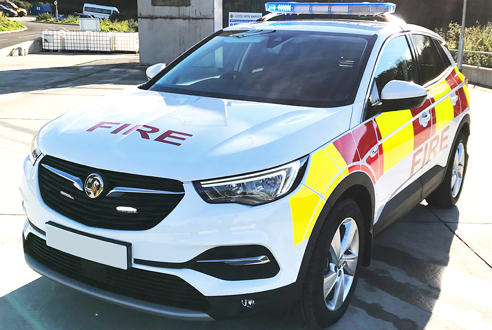 Angle view of white fire response vehicle with half lit lightbar on cemented vehicle forecourt