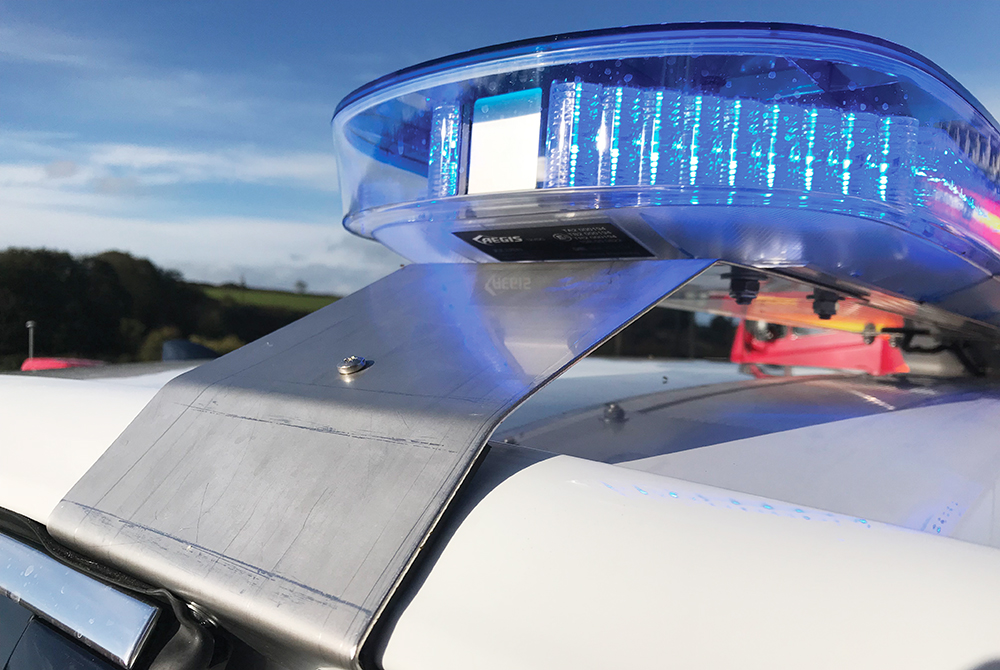 Closeup of blue lightbar mounted on white vehicle roof with rural scene and sky in background