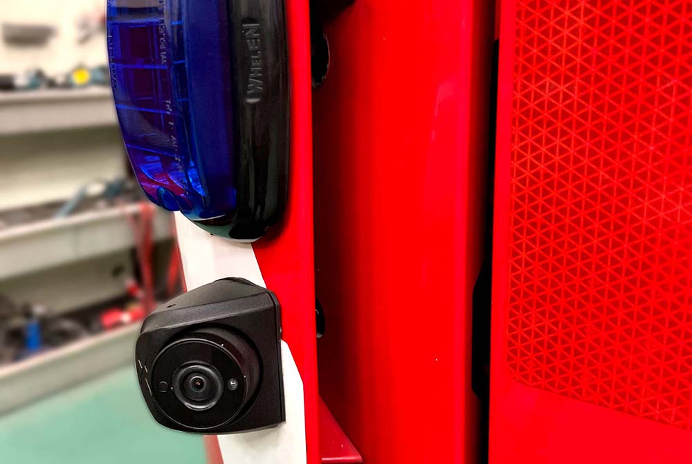 Close up of a camera mounted onto a red vehicle underneath an unlit light with blue lens with workshop environment in background