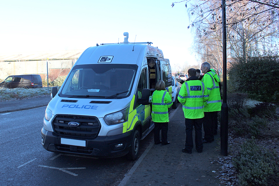 Angle View of Police Safety Camera Van Parked on Road with Group of Police Staff Crowded Around Open Side Door