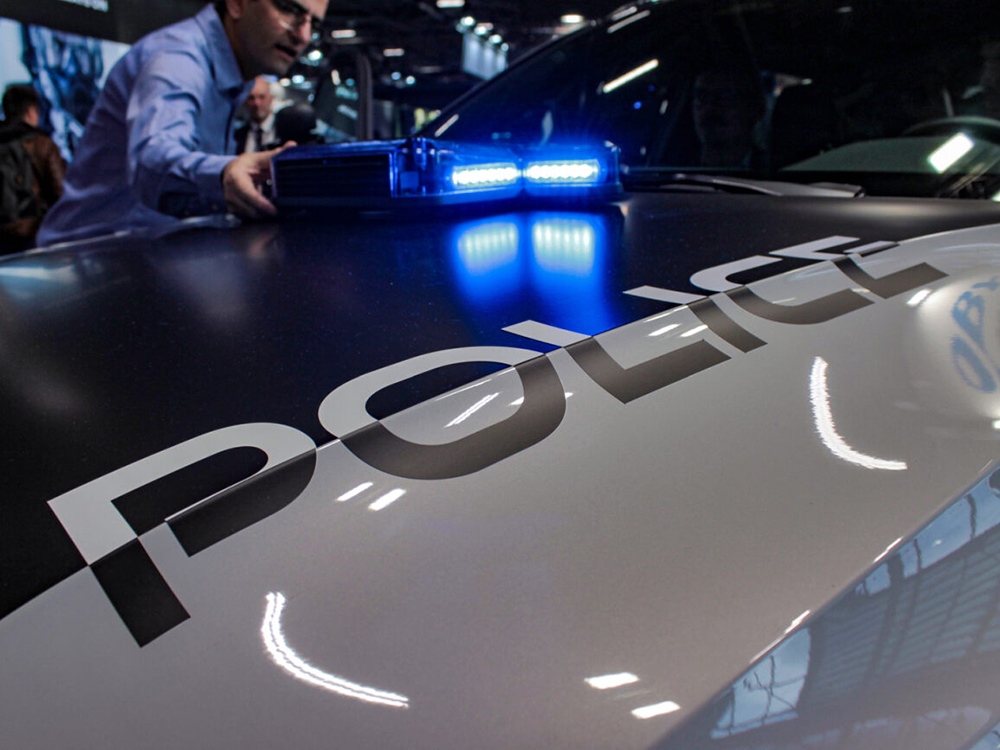 Close up of a blue lit hood mounted lightbar on a police car hood with a person bending in for a closer look.