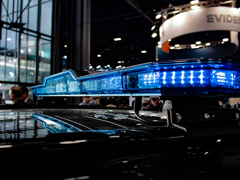 Close up of a blue lit lightbar on top of a black car roof at a busy exhibition.