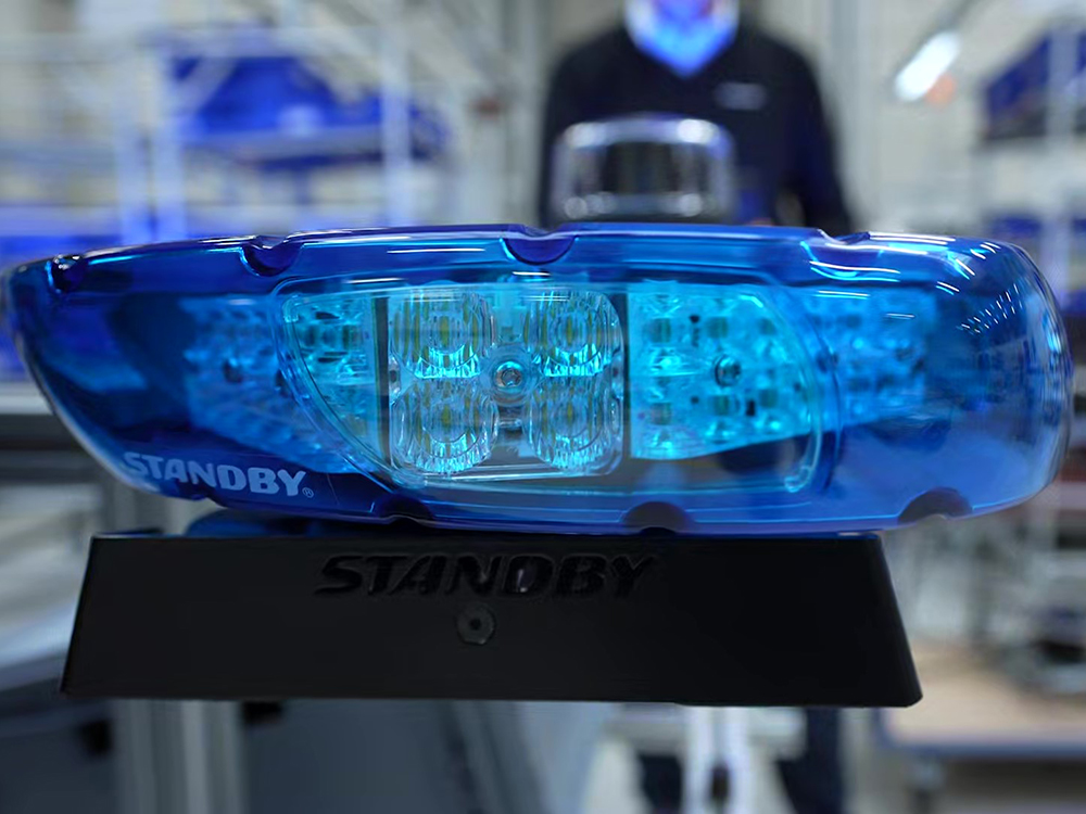 Close up of the blue lens of an unlit lightbar, side on, with someone standing out of focus in the background. The lightbar has a Standby logo on.