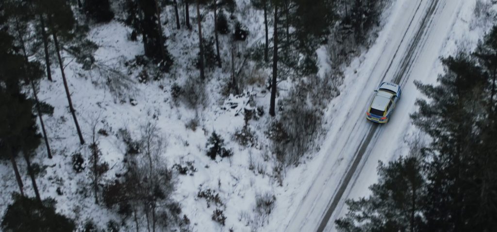 Vy från luften på en polisbil som kör på en snöig väg i skogen. Om oss