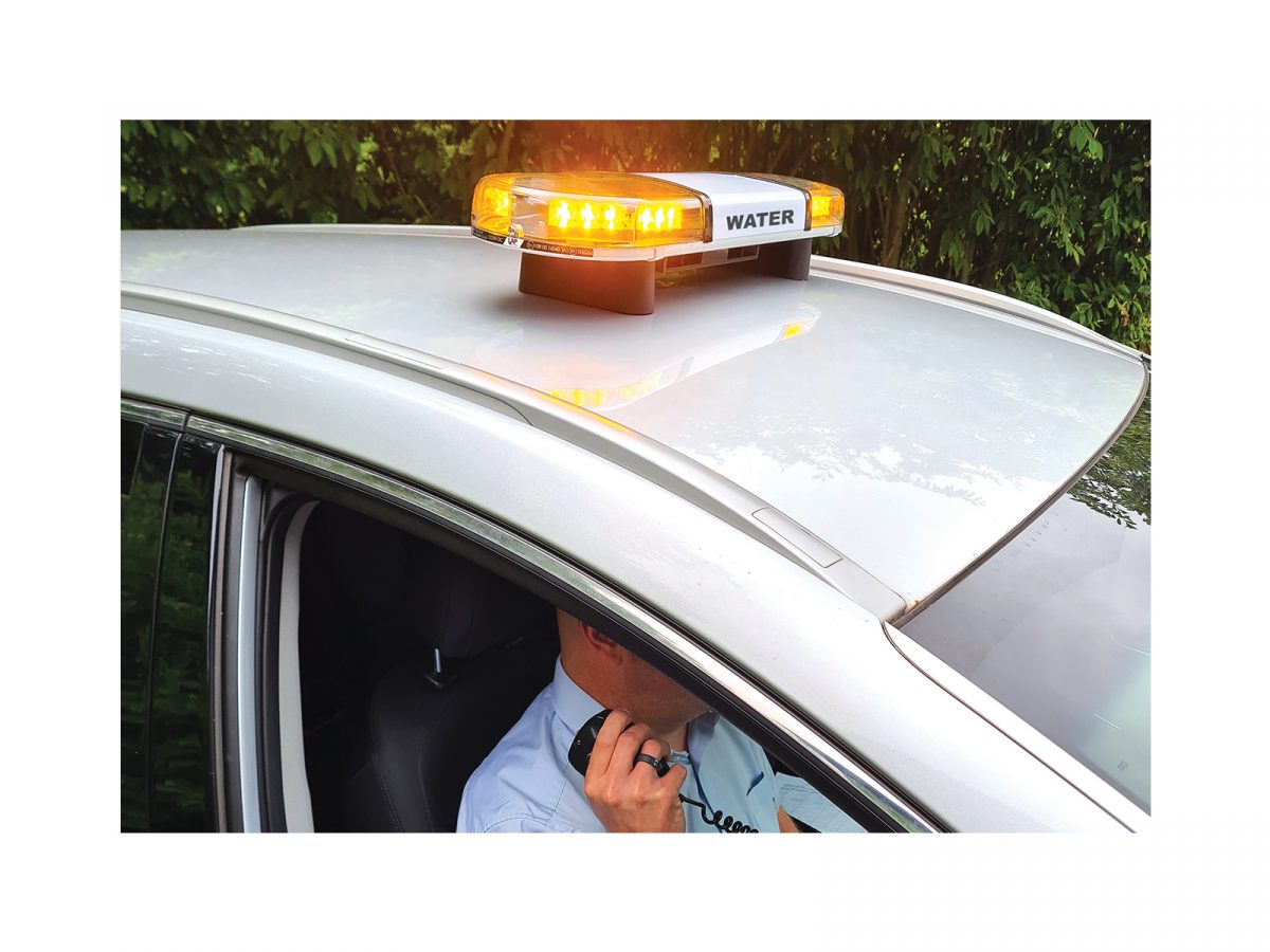 Hurricane PA Lightbar with 60 Watt Speaker Driver In Situ Angle View Lit Water Livery on Roof of SIlver Car with Handset Operator is Driving Seat