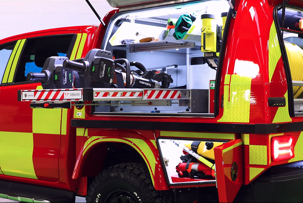 Close up of fire response vehicle with open hatches showing various pieces of equipment, lit up on the inside