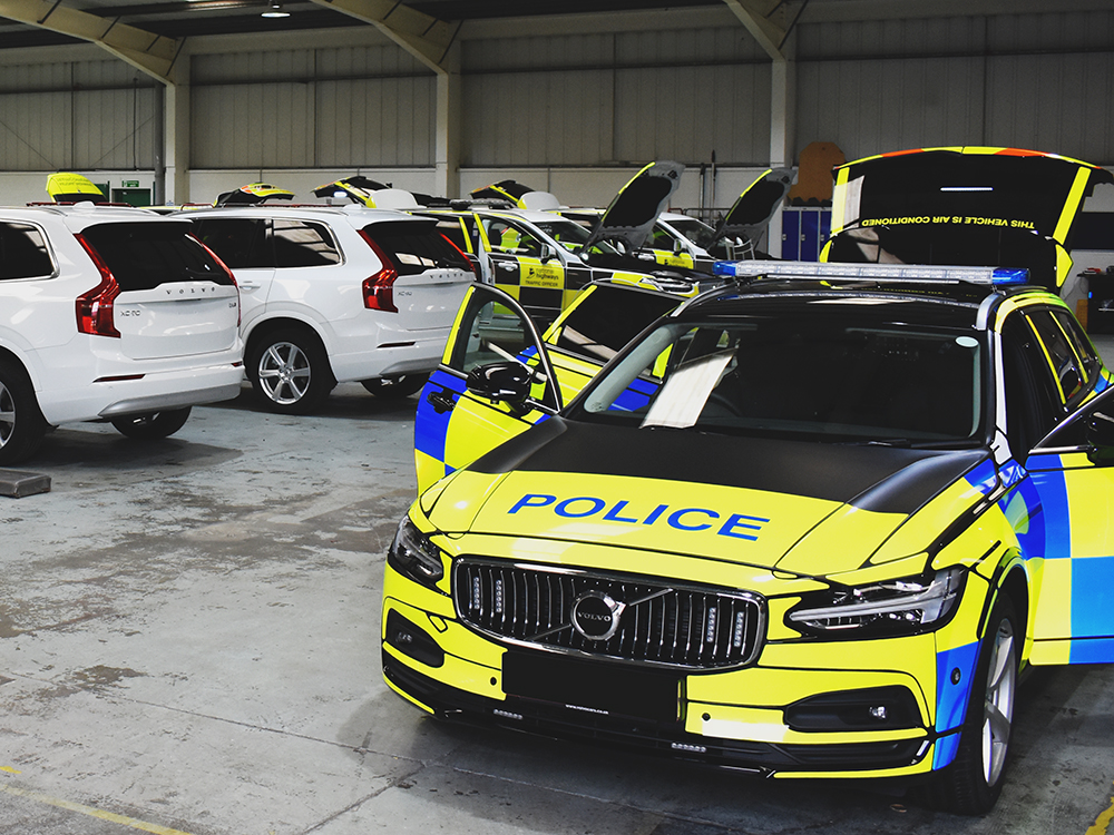 Police Vehicle in a workshop environment with doors and boot open, white Volvos in various states of completion are lined up in the background
