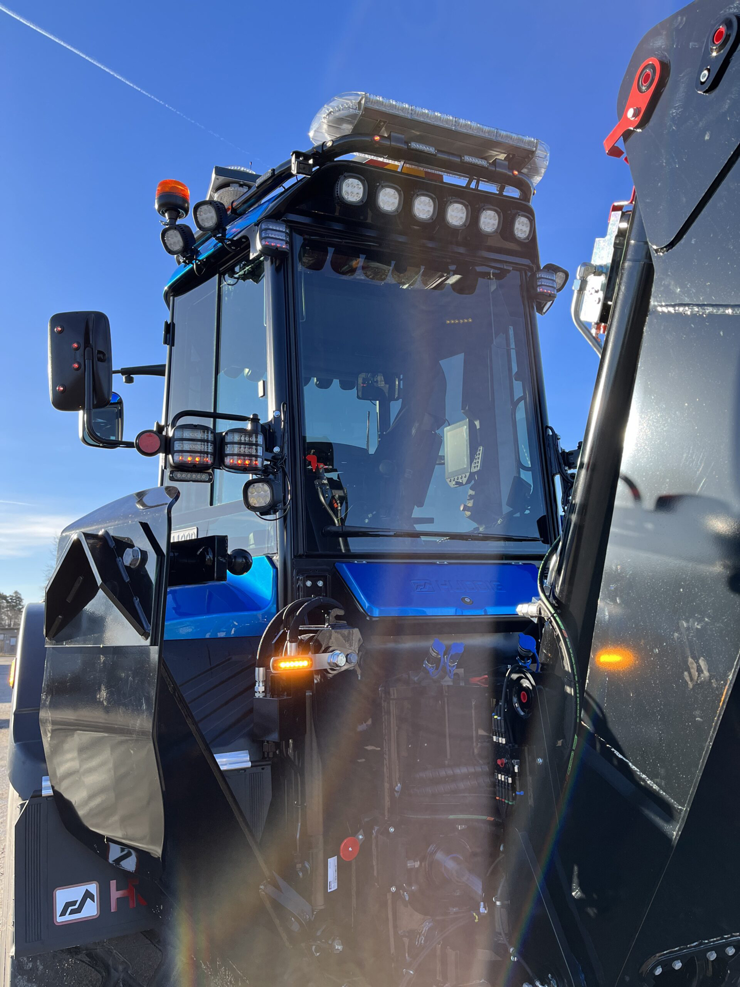 Closely Cropped Angle Shot of Blue Excavator Cab with Amber LED Modules and Unlit Lightbar Against Blue Sky Background