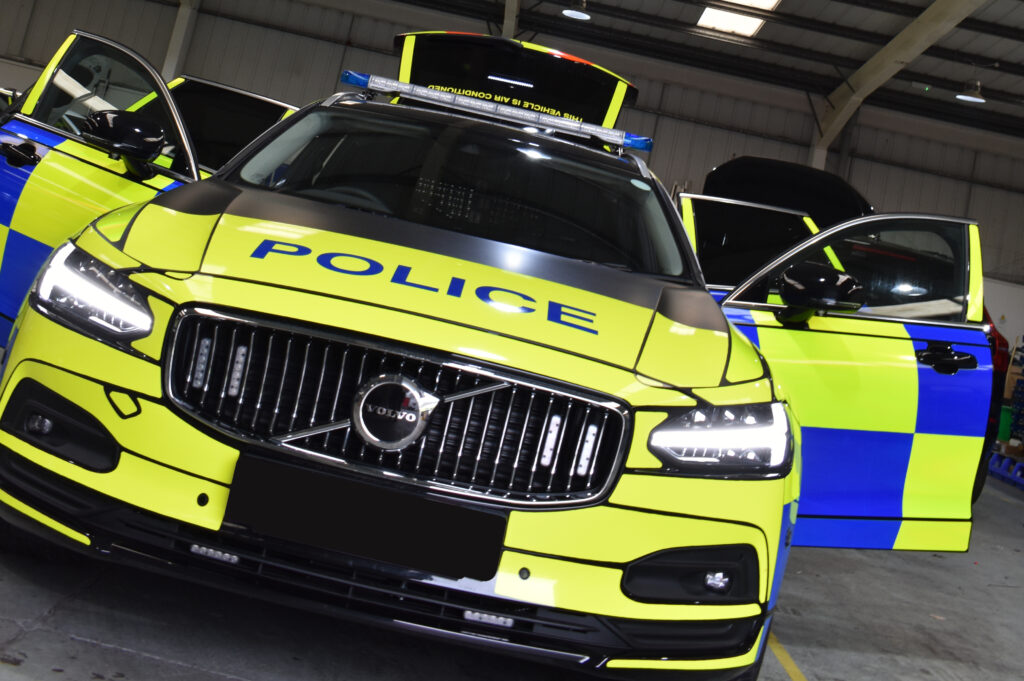 Volvo car with doors open shown at an angle with full Police livery and headlights on in workshop environment