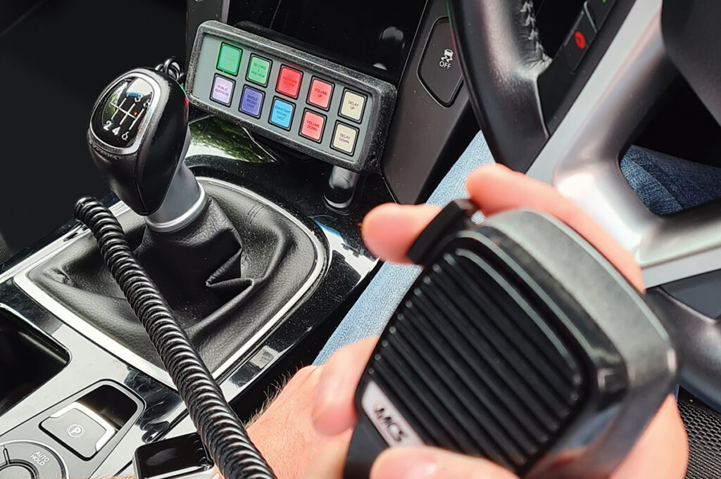 Closely Cropped Shot of Handheld Microphone Out of Focus in Foreground and Handset in Background Beneath Vehicle Centre Console