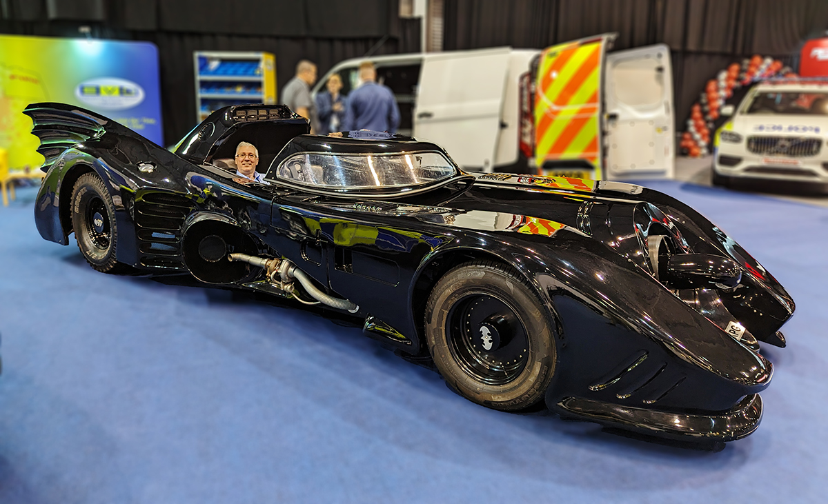 Smiling person is sitting in the Batmobile on EVO Ltd's stand at NAPFM, smiling and looking at the camera, angle view