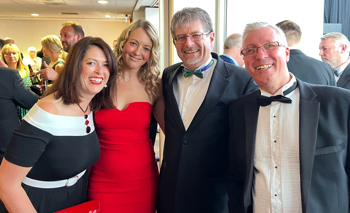 Four people dressed in evening wear are grouped together, smiling and looking at the camera