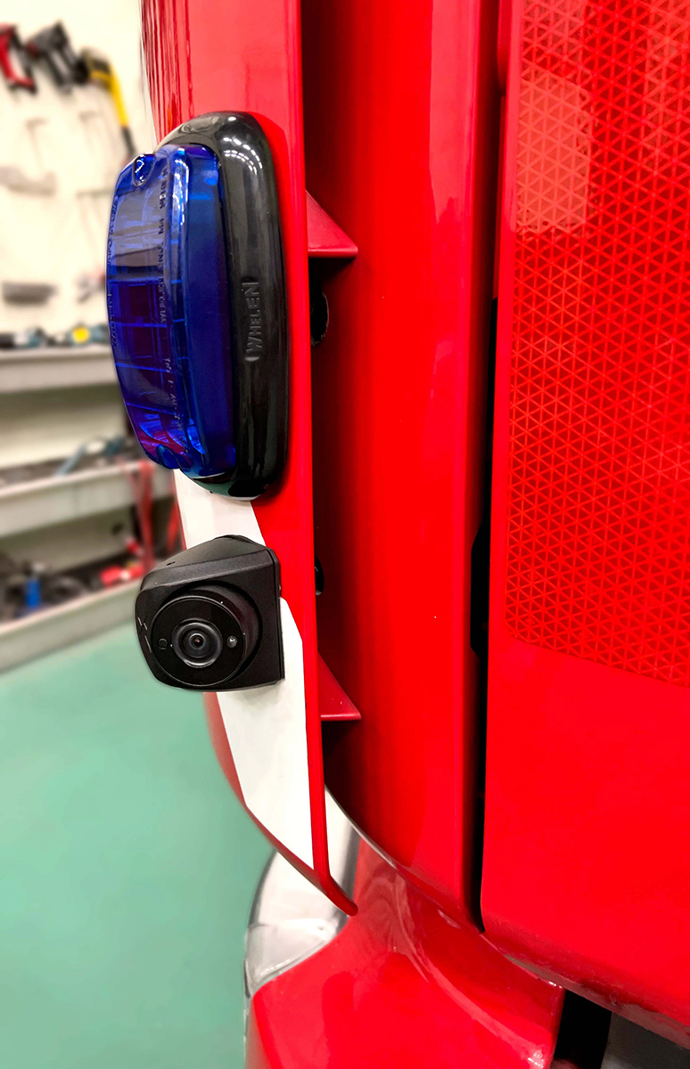 Close up of a camera mounted onto a red vehicle underneath an unlit light with blue lens with workshop environment in background