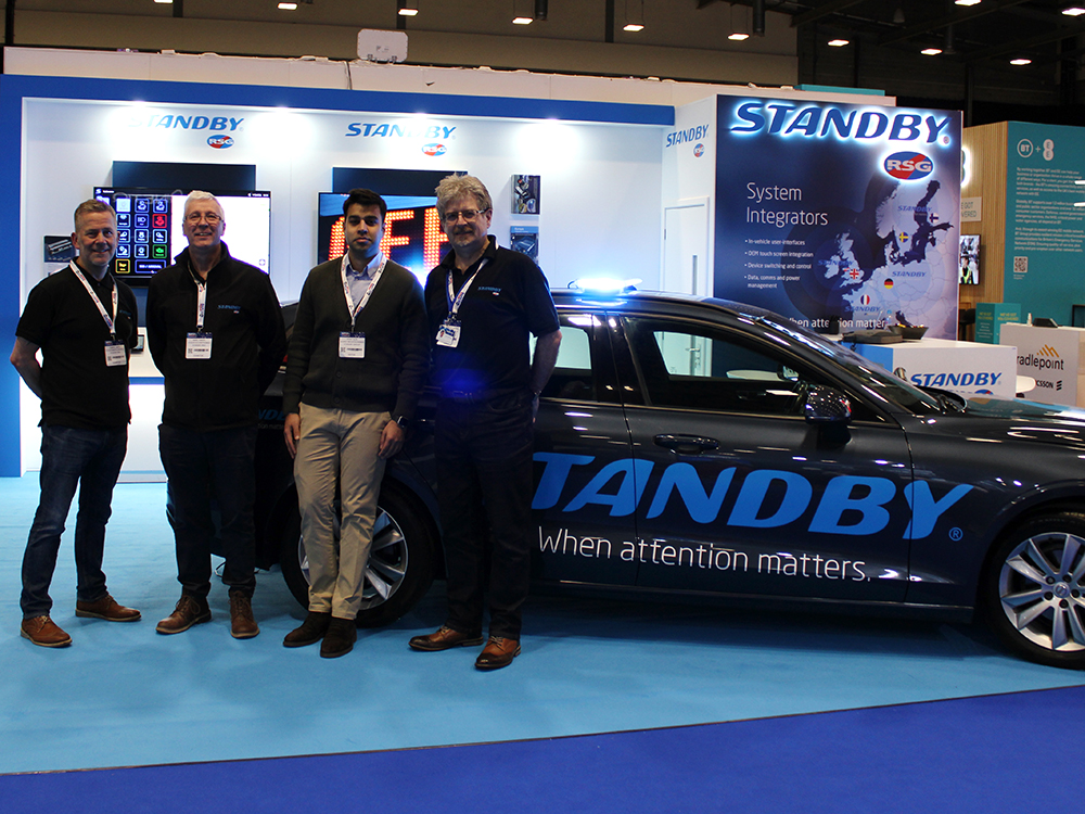Standby RSG exhibition stand with demonstration car and four Standby colleagues standing next to the boot, smiling and facing the camera.