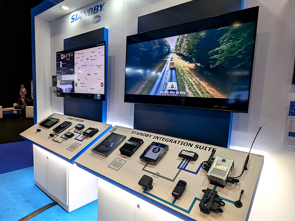 Close up of Standby RSG exhibition stand showing two screens with different video clips playing and two equipment boards, one reads CARAT System and the other reads Standby Integration Suite.