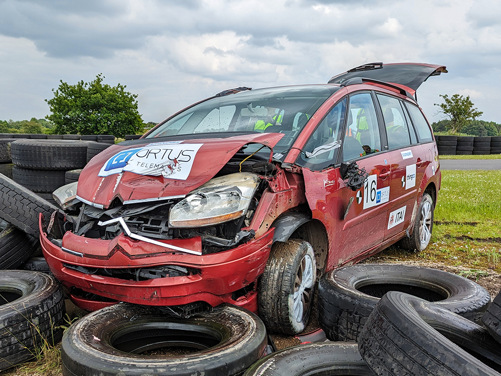 Heavily damaged red Citroen vehicle which has most of the engine bay crumpled in and the boot open, having crashed into a tyre wall at a racetrack.