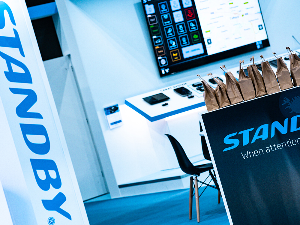 Angle view of a neat, modern, white exhibition stand with white and blue decor and brown kraft branded paper bags stacked on the desk.