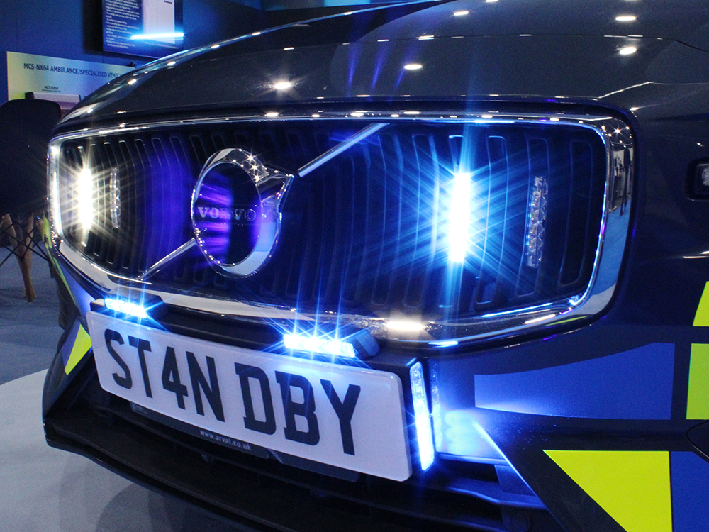 Close up of a grille of a Volvo vehicle with a license plate that reads 'ST4N DBY' and grille and license plate lights in blue and white.