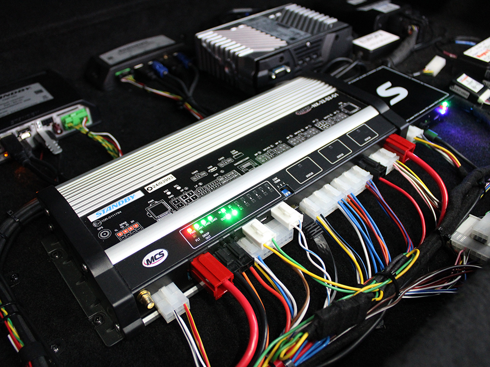 Close up angle shot of a boot installation with an MCS-32 connected to other various pieces of equipment by colourful wires. Small LED indication lights are lit up across the equipment.