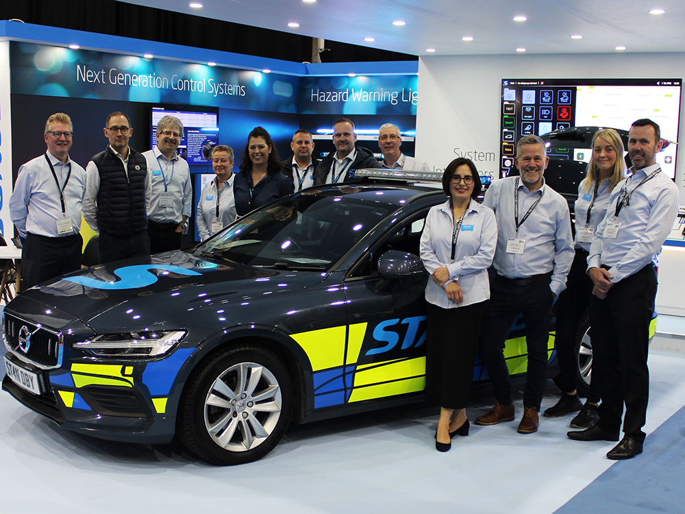 Shot of Standby staff gathered around a Standby branded emergency response vehicle on an exhibition stand with lights and screens.