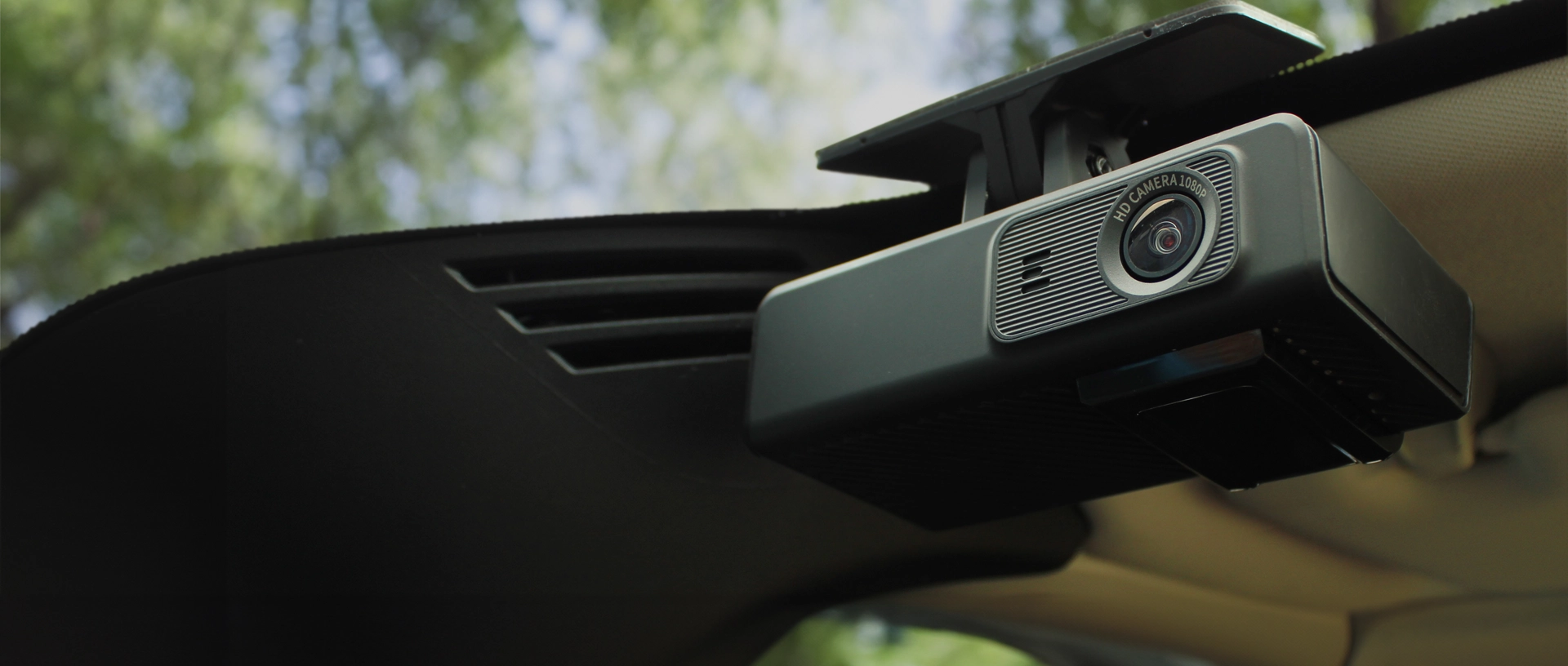 Low angle view of a dash cam mounted on a car windshield with an out of focus foliage and sky view through the glass