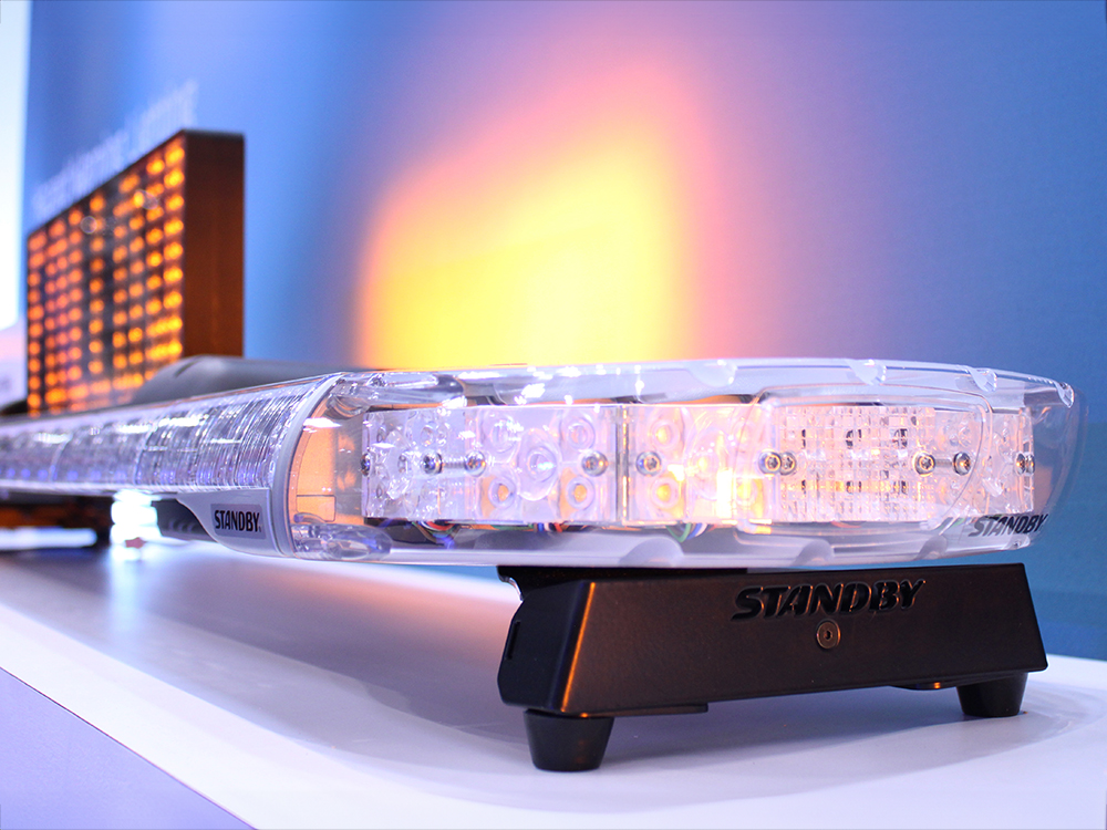 Closely cropped angle view of an emergency lightbar on a white shelf with an amber matrix sign mounted on the top reading 'Police'. The amber reflects on a darker background.