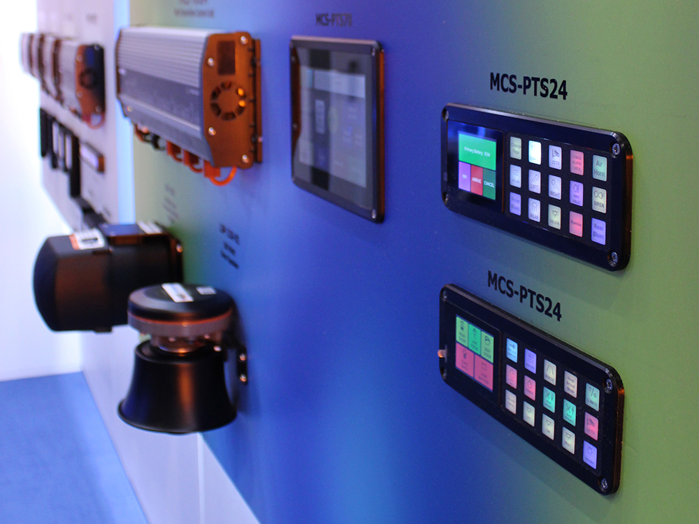 Closely cropped angle view of various touchscreen and button controllers with other emergency equipment mounted on multi colour display boards at an exhibition.