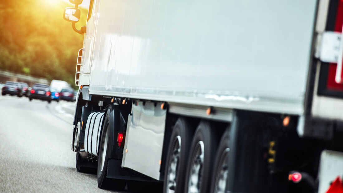 Rear side angle of a commercial vehicle driving down the road, closely cropped with some vehicles omn the road in the distance.