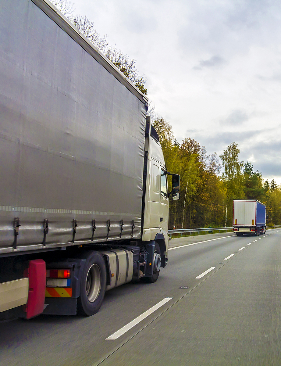 Commercial vehicle driving on the lefthand side of the motorway, side rear angle, another CV ahead.