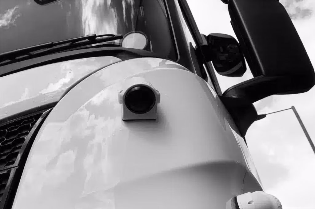 Close up shot of Oculux Camera mounted next to the grille on an HGV in black and white shown at an angle.