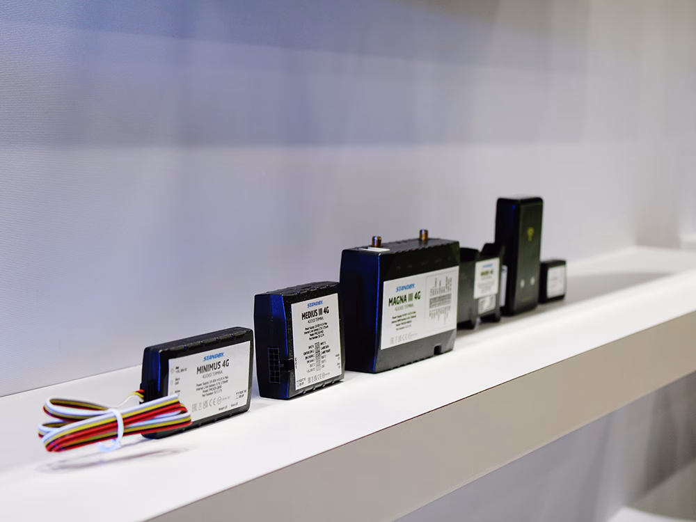 Angle view of Standby UK Fleetmotus Telematics devices lined up on a white shelf against a white wall.