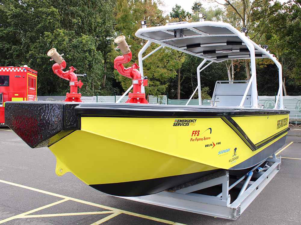Yellow Fire and Rescue boat outside at the Emergency Services Show 2025 with various contributor logos including Standby UK's on the side as well as Emergency lighting around the top.