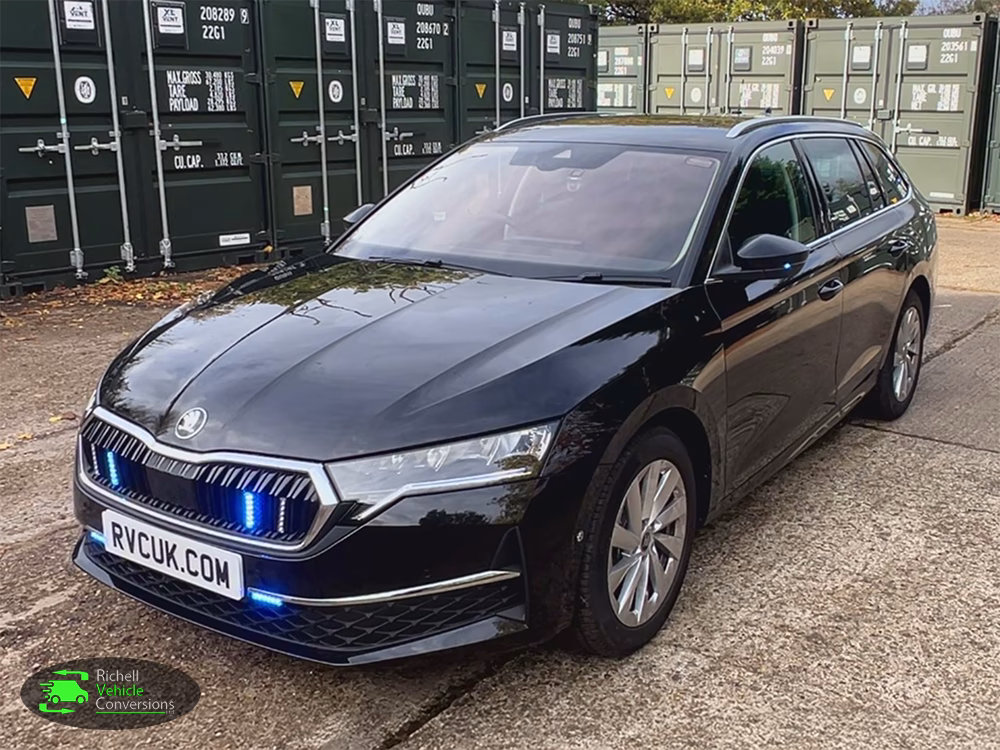 RVC Skoda Octavia Driver Training Vehicle shown at an angle with blue lights parked on a concrete surface in front of large green shipping containers.