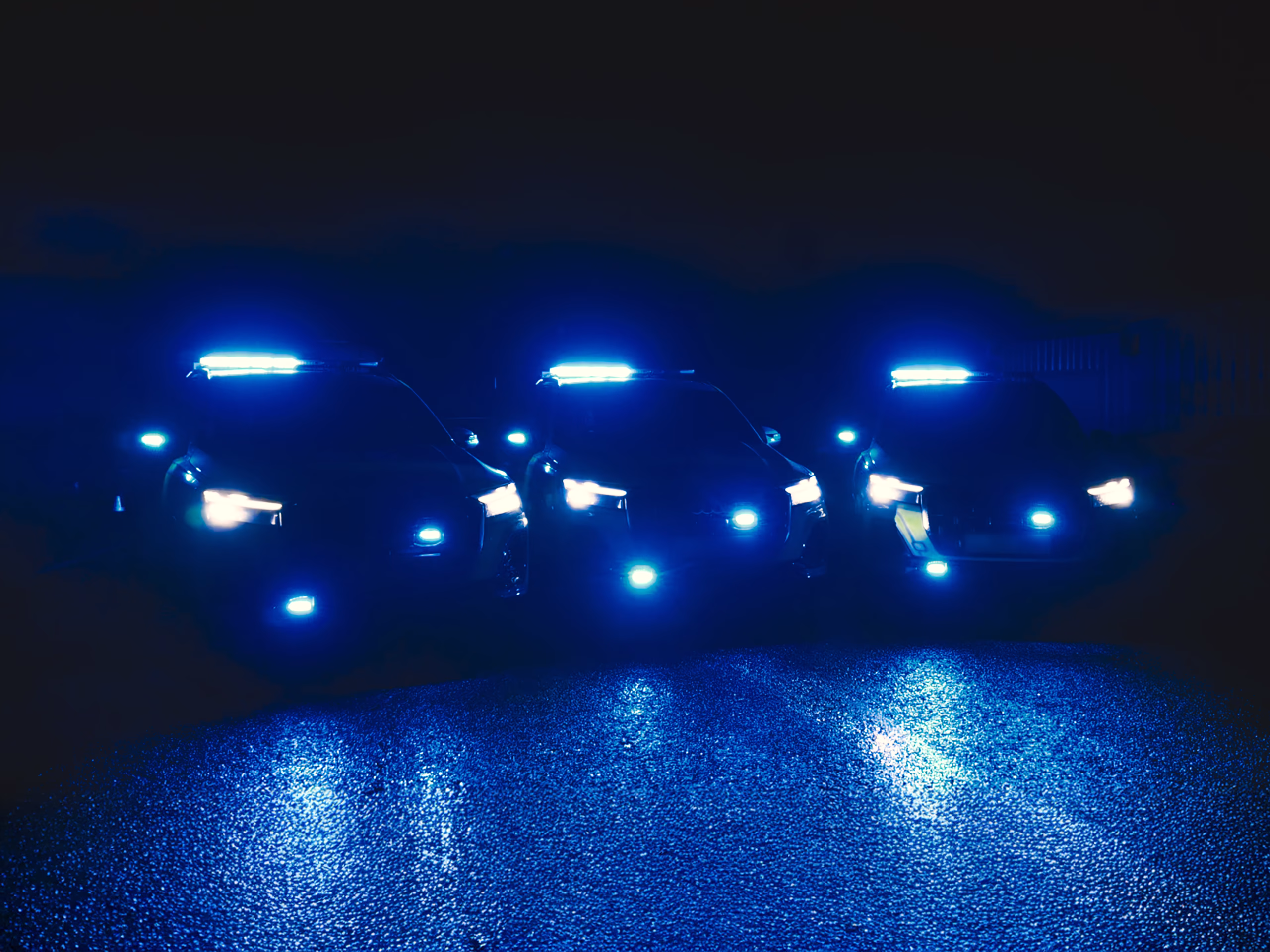 Three Police cars at night parked in a row each with identical blue lights illuninated on a wet carpark demonstrating the Standby UK Sync & Breathe MCS-NX function