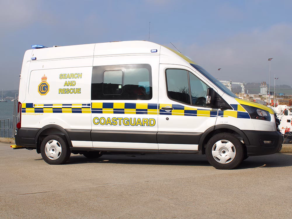 HM Coastguard Ford Transit OSV with lit blue lights parked in a harbour on a bright day