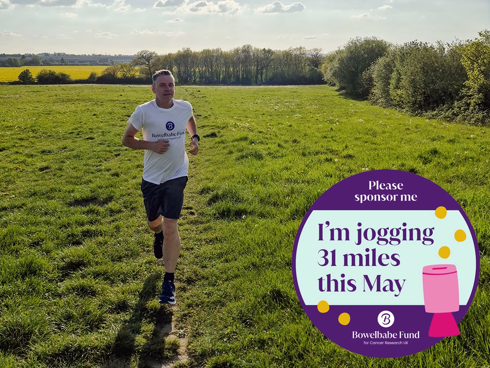 Standby UK's General Production Operative Darren Challinor wearing a white Bowelbabe tshirt and running gear, runs towards the camera in a green field on a sunny day with BowelBabe funding sticker to bottom right corner