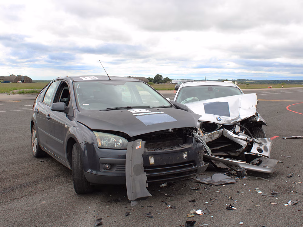 Staged crash of a dark and light car, both with heavy damage, taken on an airfield runway at ITAI Crash Day 2026