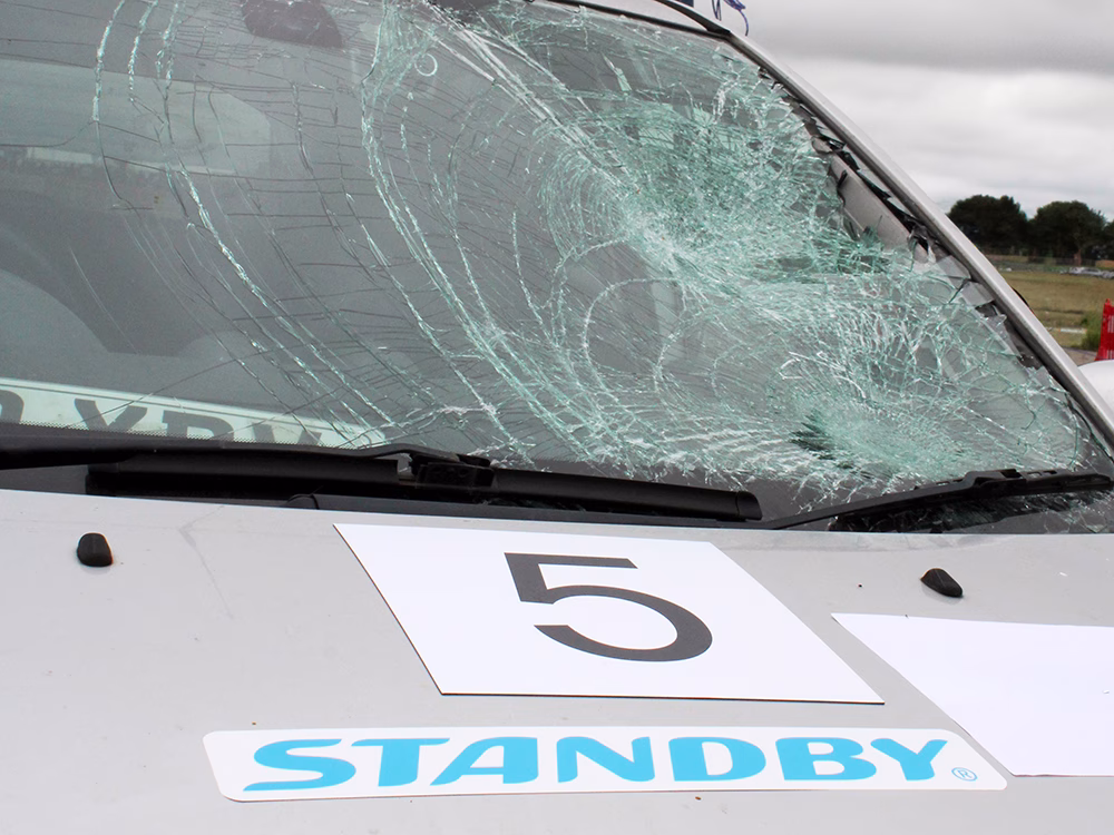 Close up of silver vehicle with smashed windscreen and Standby logo on bonnet at ITAI Crash Day 2026