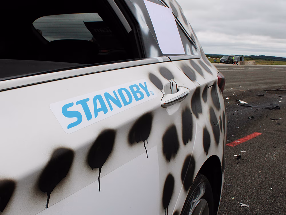 Close up of a Standby sticker on the rear door of a white vehicle with black spray painted spots taken on an airfield runway at ITAI Crash Day 2026