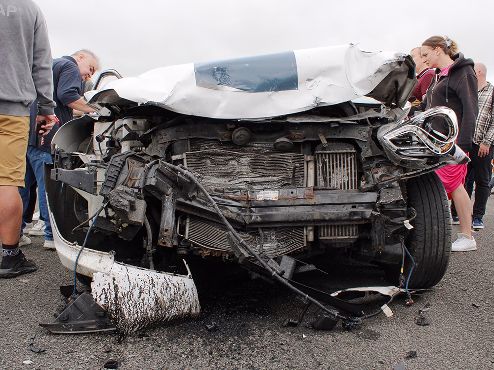 Heavily damaged front end of a silver vehicle after a staged crash taken on an airfield runway and surrounded by onlookers at ITAI Crash Day 2026