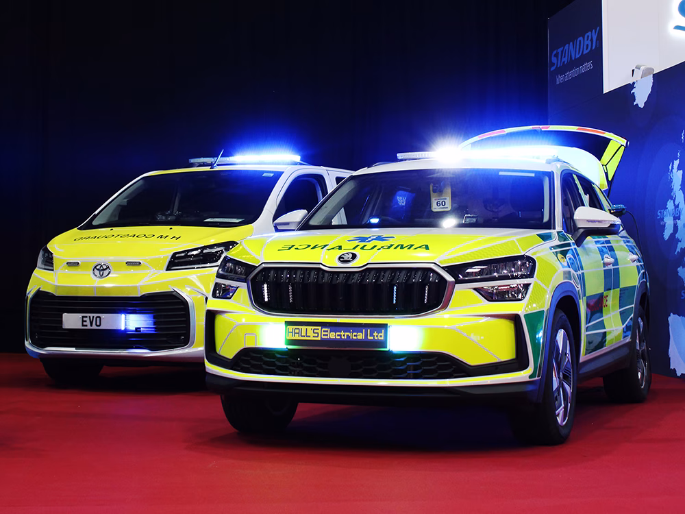 Hall's Electrical Skoda Kodiak Rapid Response Vehicle and EVO Coastguard Toyota Proace Verso EV Personnel Carrier parked in the gangway next to the Standby UK stand with emergency lights lit, on a red carpet with black curtains and a blue map graphic with the Standby logo and tagline on the side of the stand.