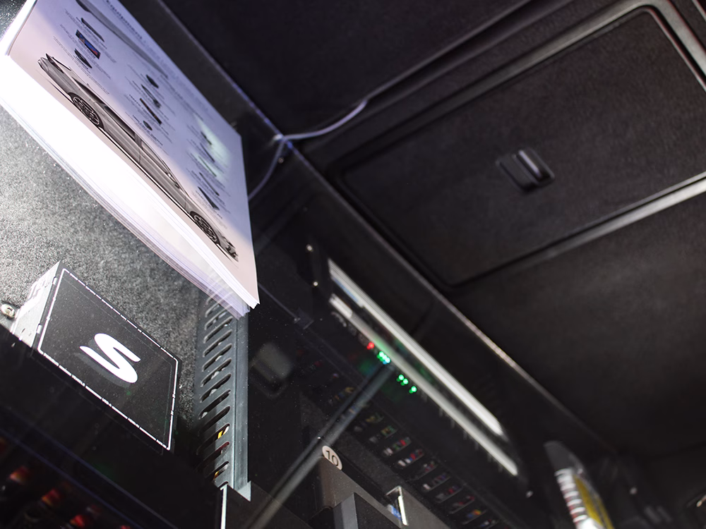 Angled shot of a boot installation including a Standby UniBox and MCS-NX32 under perspex on a South Wales Police Cupra Leon Estate RPU converted by Elite Solutions at NAPFM 2026. The compartments are lit up so that the equipment is visible. A kit list is laminated and placed on top of the perspex.