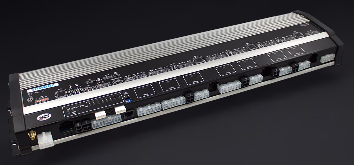 An MCS-NX64 Standby vehicle control unit, an electronic module with numerous input/output ports and connectors for vehicle equipment, shown at an angle against a black background.